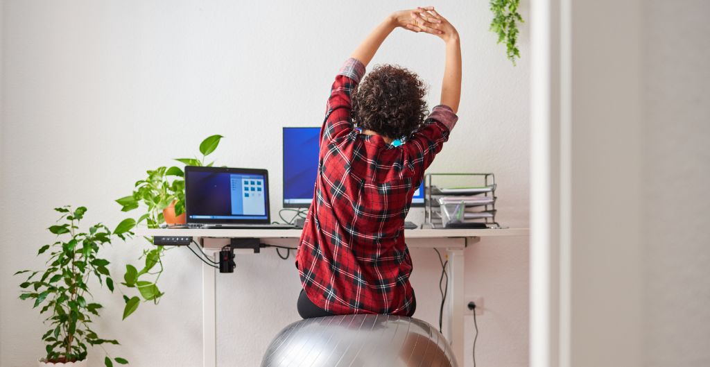 Brunette woman working from a home office sitting on an exercise ball and stretching