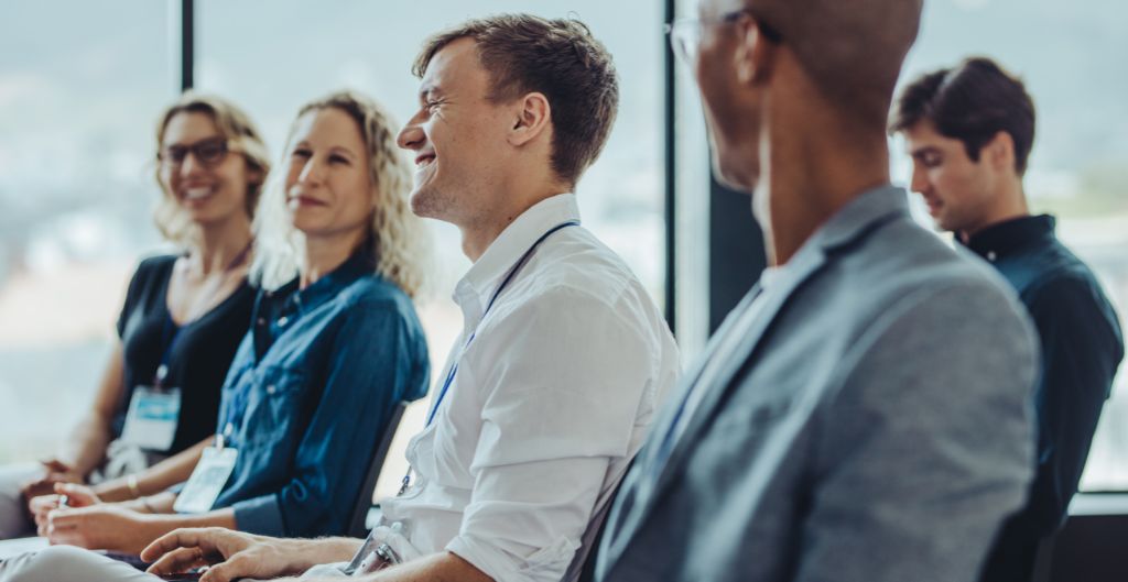 Group of four colleagues sitting in a row at a meeting smiling